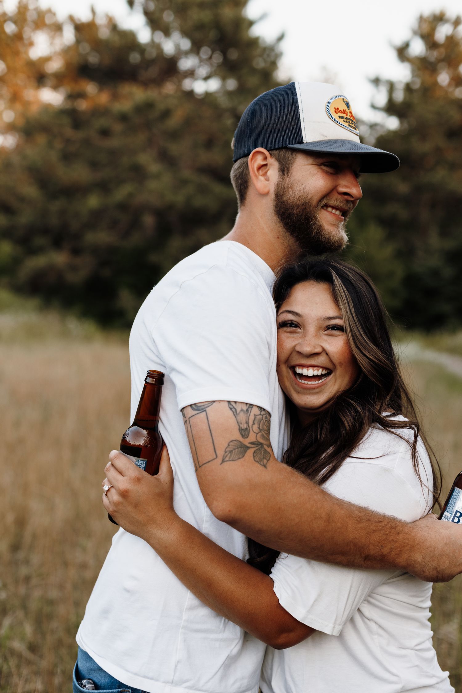Couple sharing a candid laugh while embracing in a field at sunset.