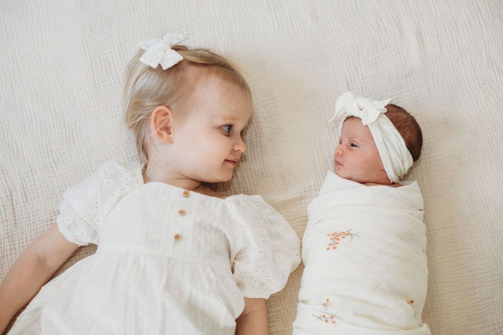 Newborn baby in white clothing resting peacefully on white bedding.