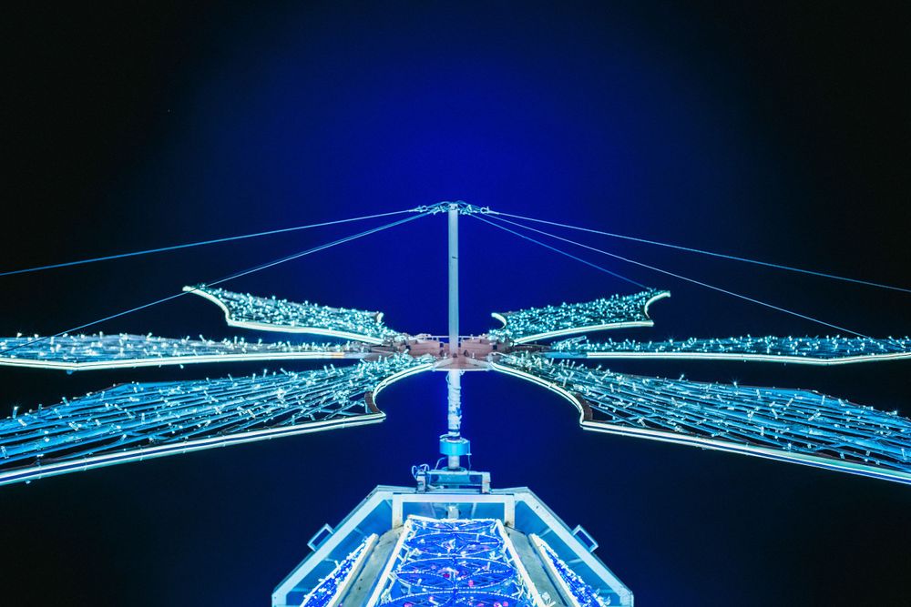 Geometric blue LED light installation resembling abstract wings against a dark background.