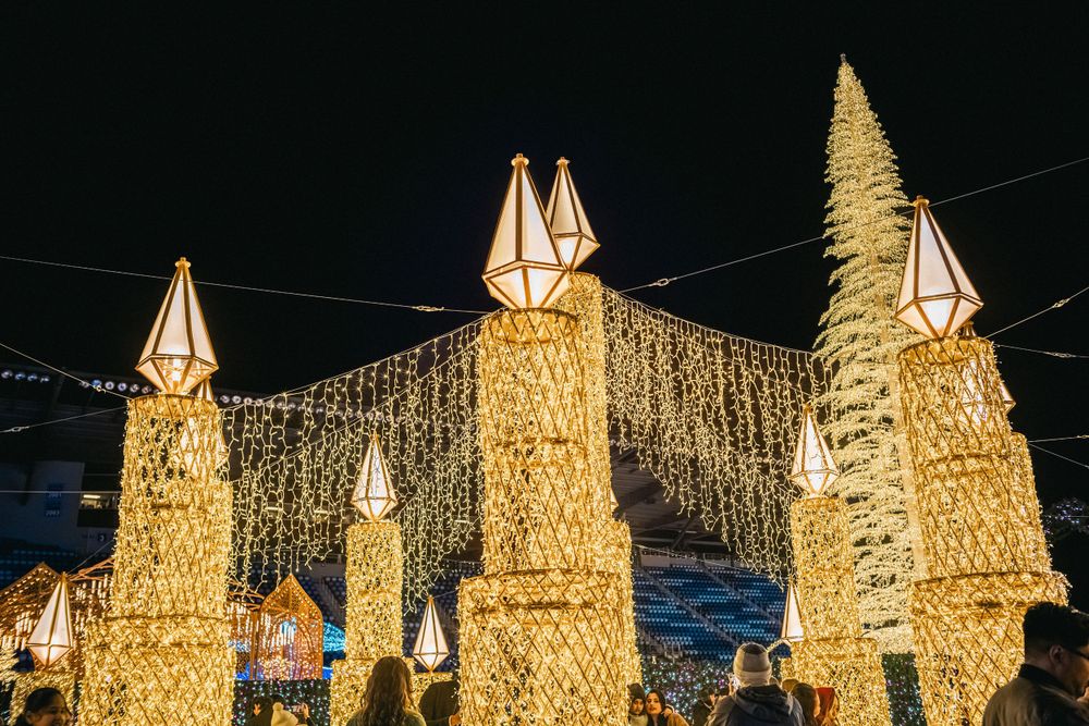 Illuminated golden architectural structures with lantern-style tops create a magical holiday display at night.