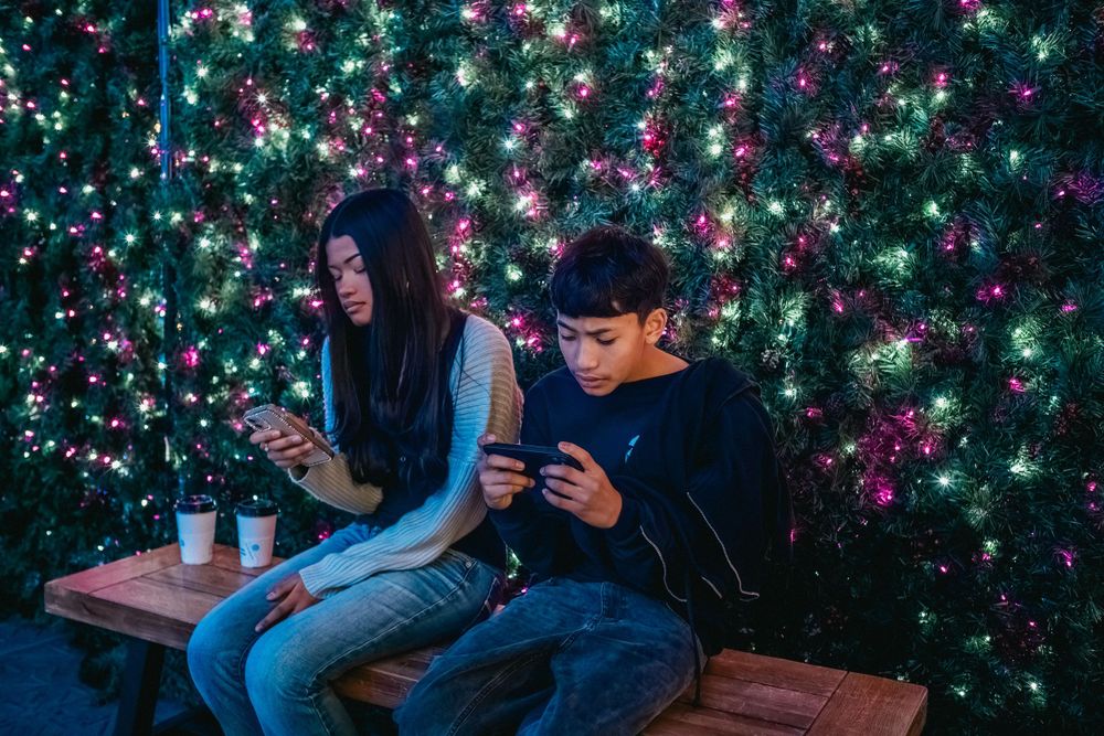 People sitting on bench against wall of twinkling pink and green holiday lights.