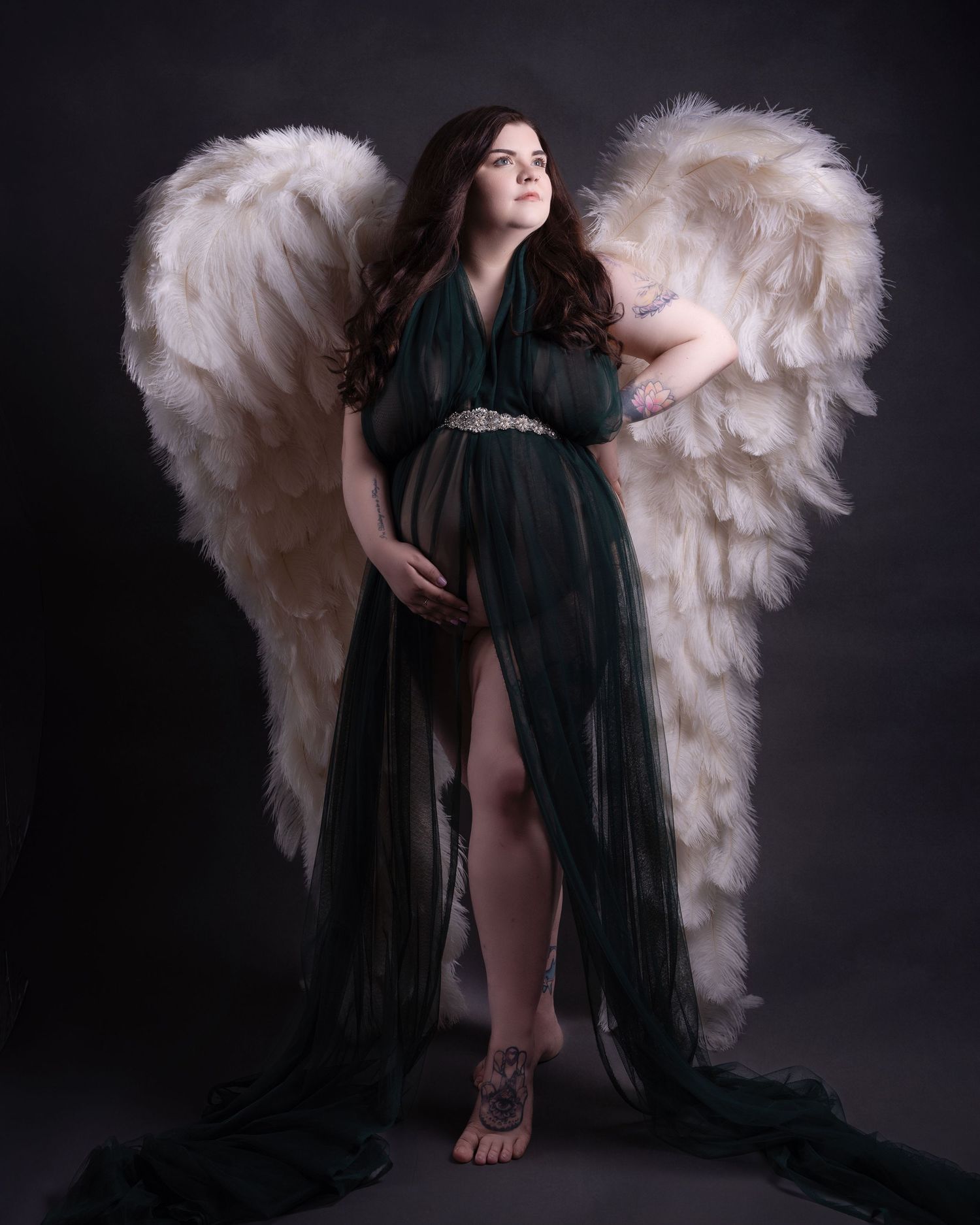 Maternity portrait with large white angel wings and emerald green flowing dress.