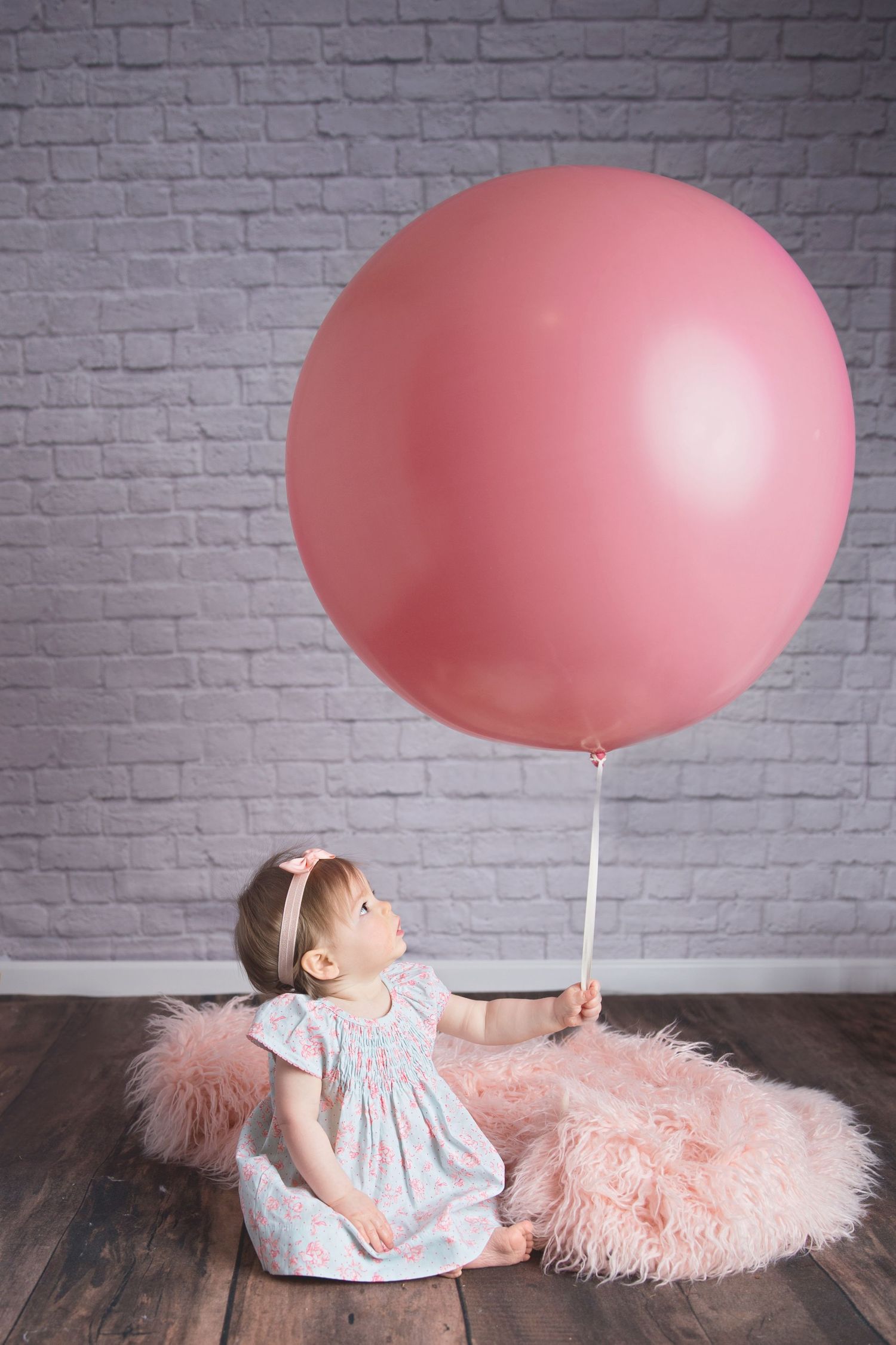 Creative baby photo series with large pink balloon against brick wall backdrop.