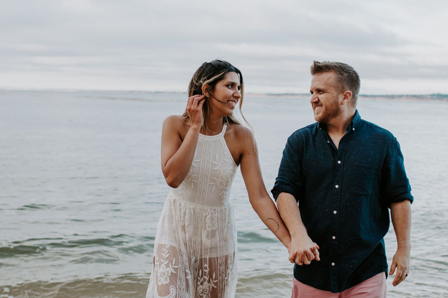 Couple walking together along a scenic beach shoreline with waves crashing behind them.