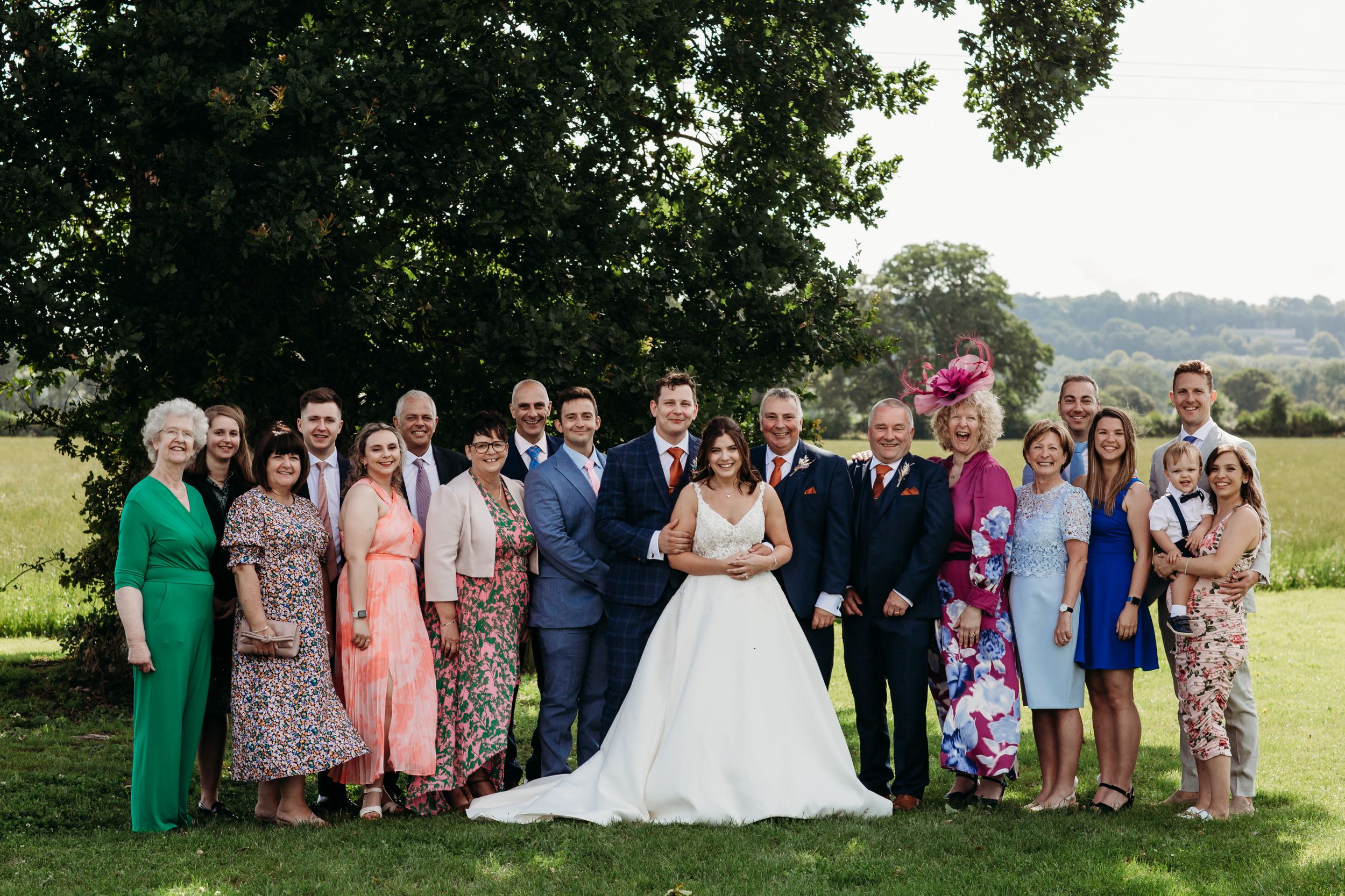 Large family wedding portrait taken outdoors with diverse attire and colorful dresses.