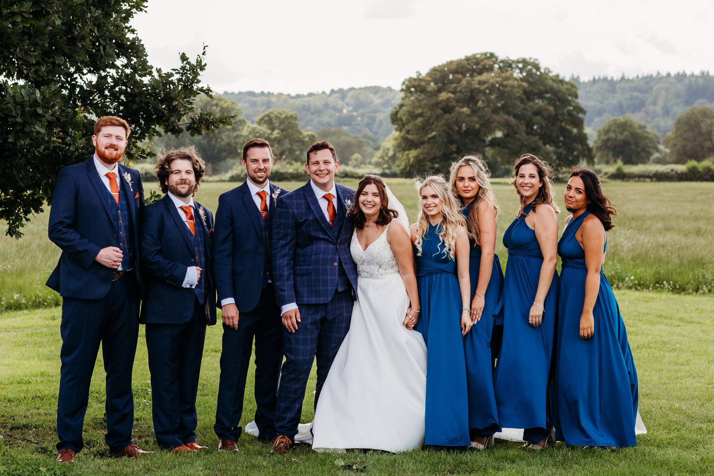 Wedding party poses outdoors with bridesmaids in royal blue dresses and groomsmen in navy suits.