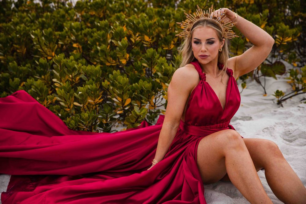 Red flowing dress spreads across sand during beach sunset photoshoot.