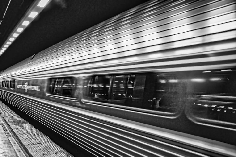 Black and white motion blur of subway train moving through underground station.