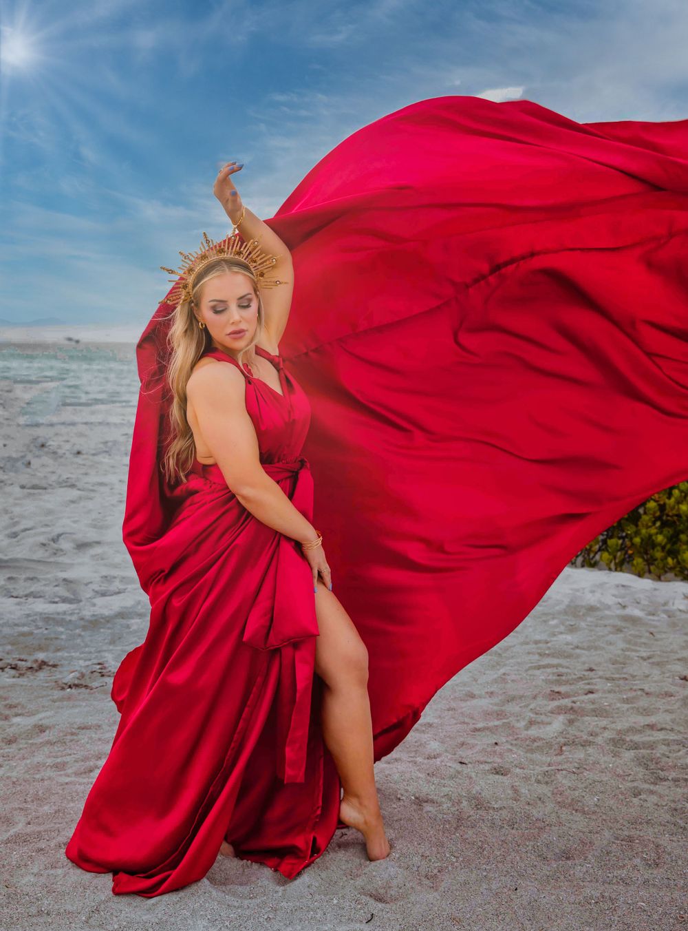 Model in red gown creates dynamic movement poses on sandy beach at sunset.