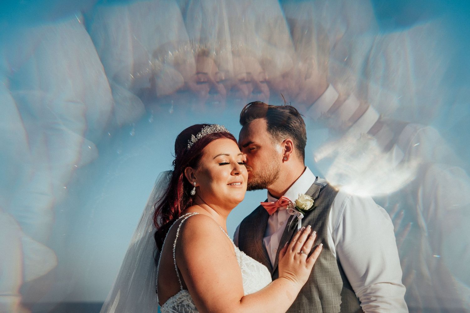 Artistic wedding portrait showing couple in close embrace against blue sky backdrop.