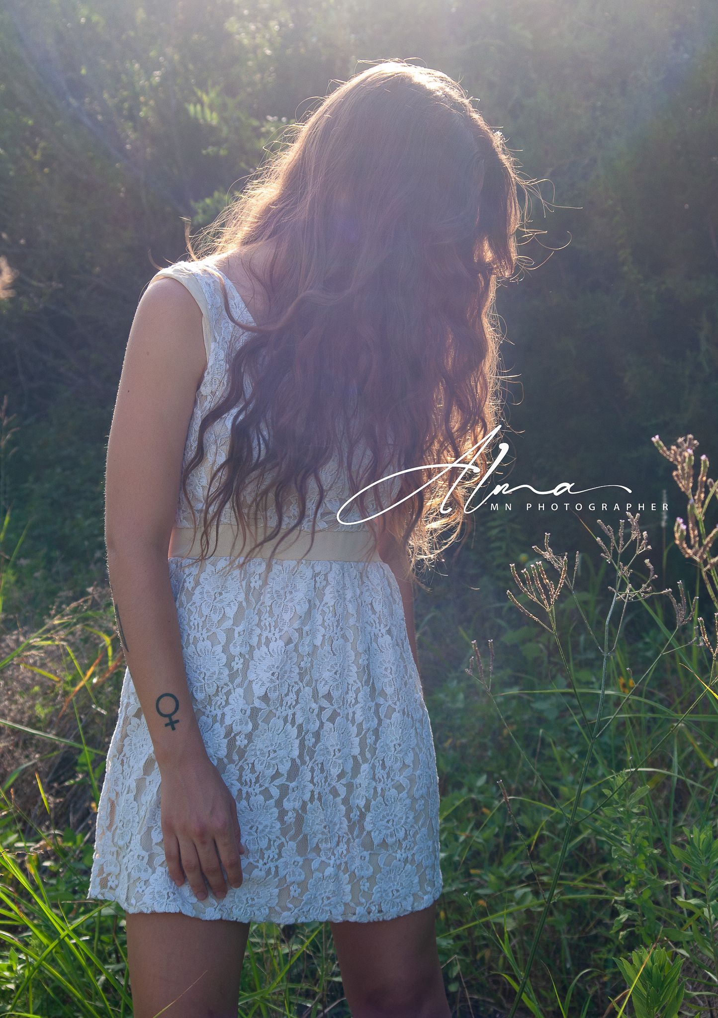 Back view portrait in white lace dress amid summer wildflowers and natural lighting.