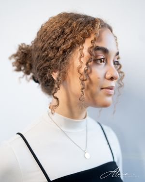Profile portrait with natural curly hair in updo wearing white turtleneck and black strap.