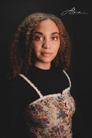 Portrait in black turtleneck and floral top with natural curls against dark background.