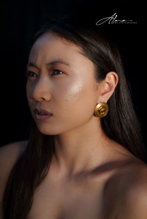 Side-lit portrait showcasing elegant gold earring and sleek dark hair against black background.