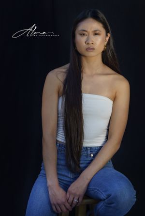 Studio portrait against black background featuring white top and long dark hair.