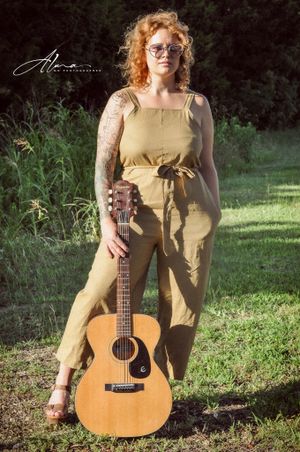 Summer portrait with acoustic guitar wearing yellow jumpsuit in garden setting.