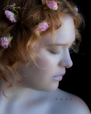 Dreamy profile portrait with pink flowers in curled hair against dark background.