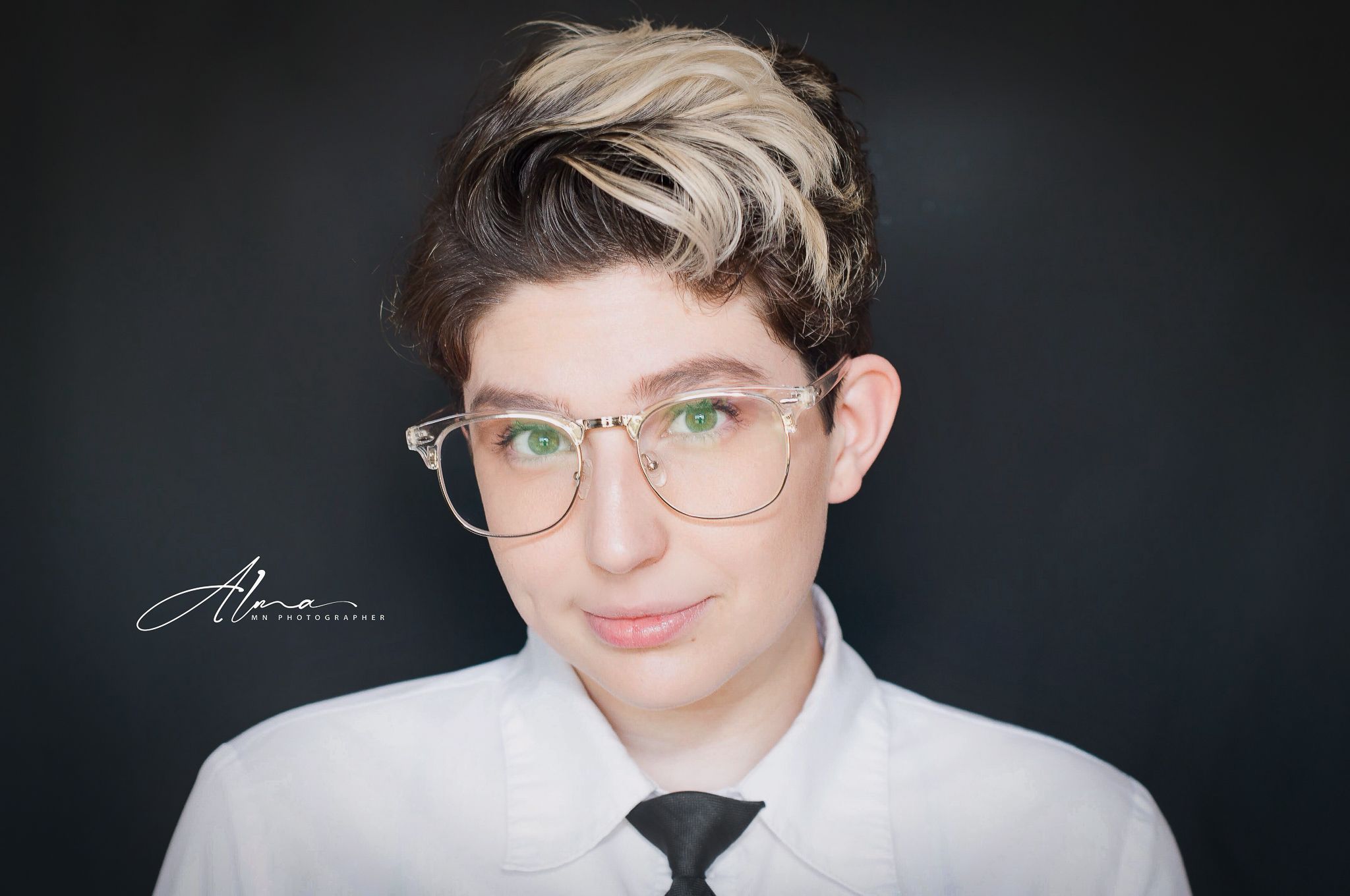 Professional headshot against dark background showing glasses and white formal attire.