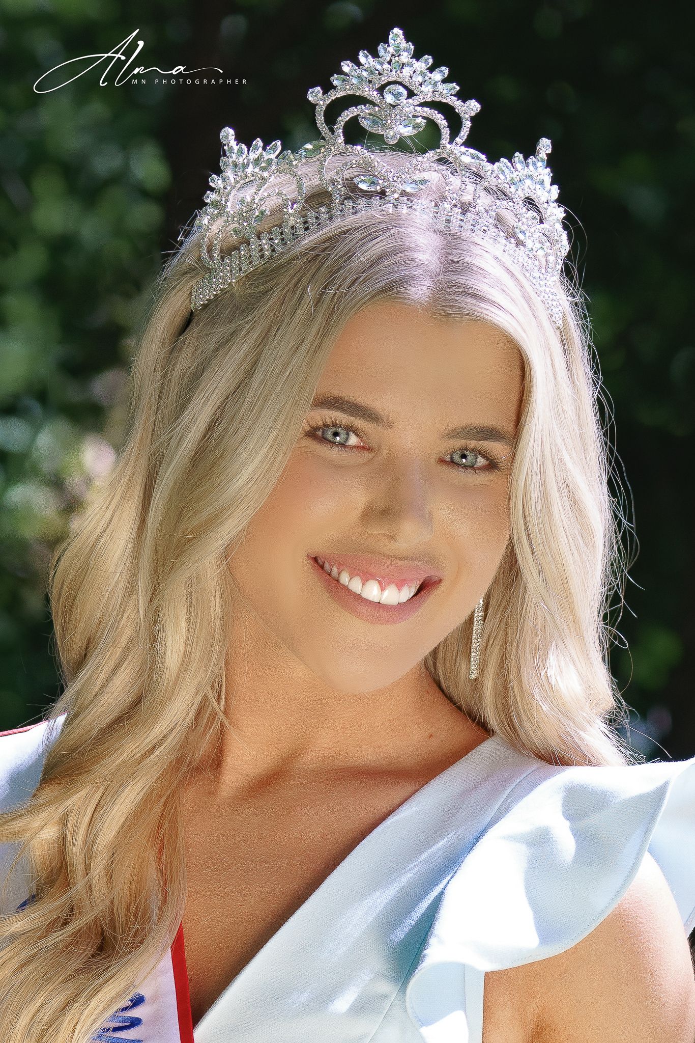 Elegant crown tiara with pearls and crystals photographed outdoors with natural greenery background.
