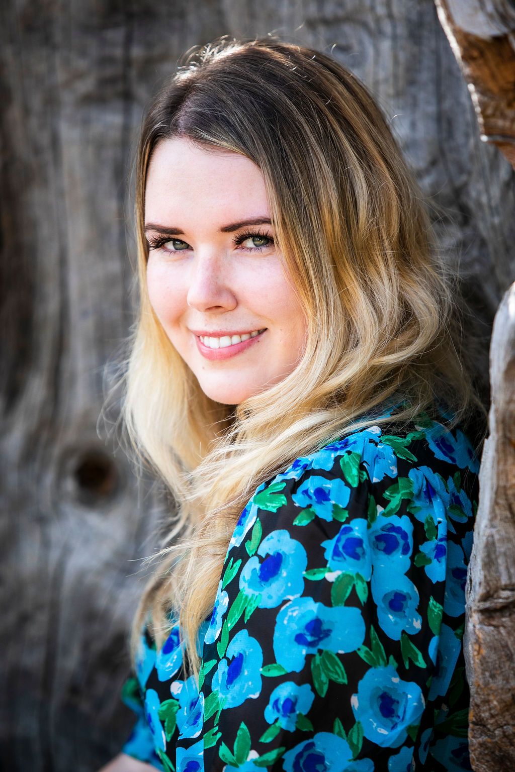 Portrait of someone in a blue floral dress smiling against a rustic wooden background.