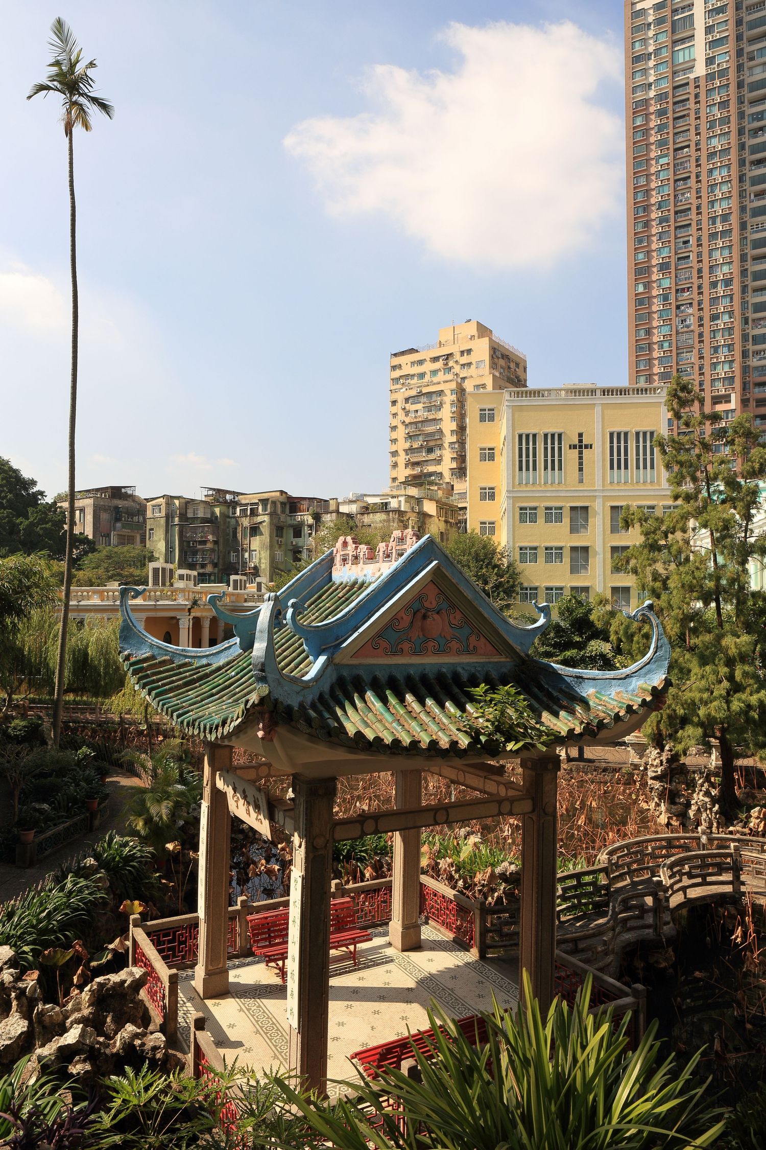 Traditional Chinese pavilion in garden with modern high-rise buildings in background.