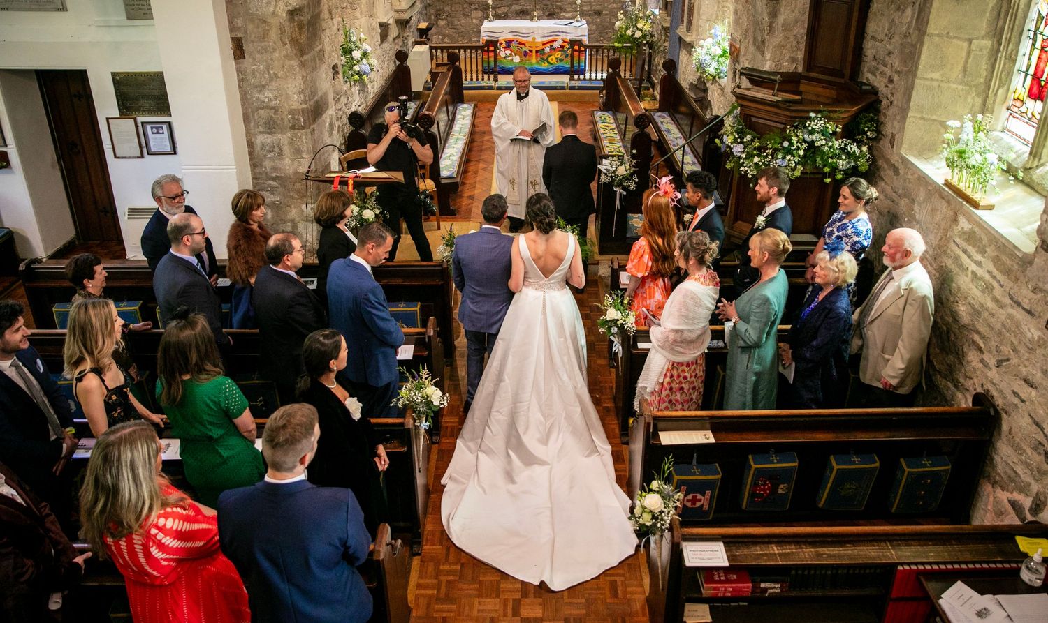 Wide view of wedding ceremony in historic stone church with guests seated in wooden pews.