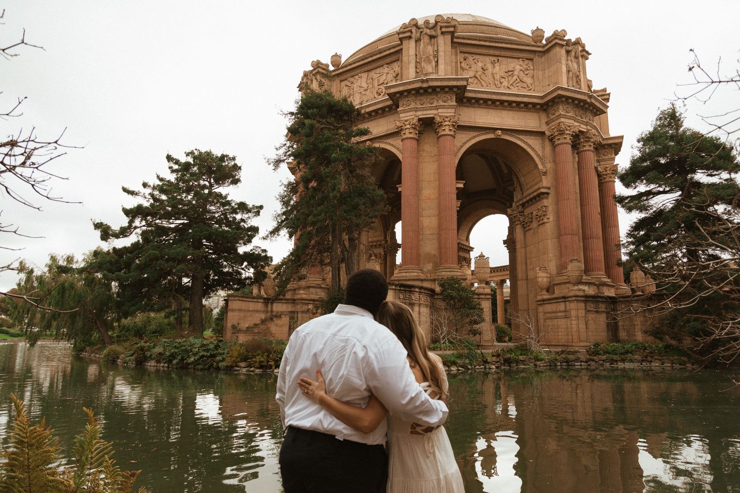 Couple embracing at Palace of Fine Arts with reflection in pond.