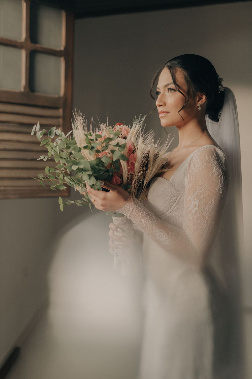 A bride in an elegant white dress holds a bouquet of mixed flowers and greenery.