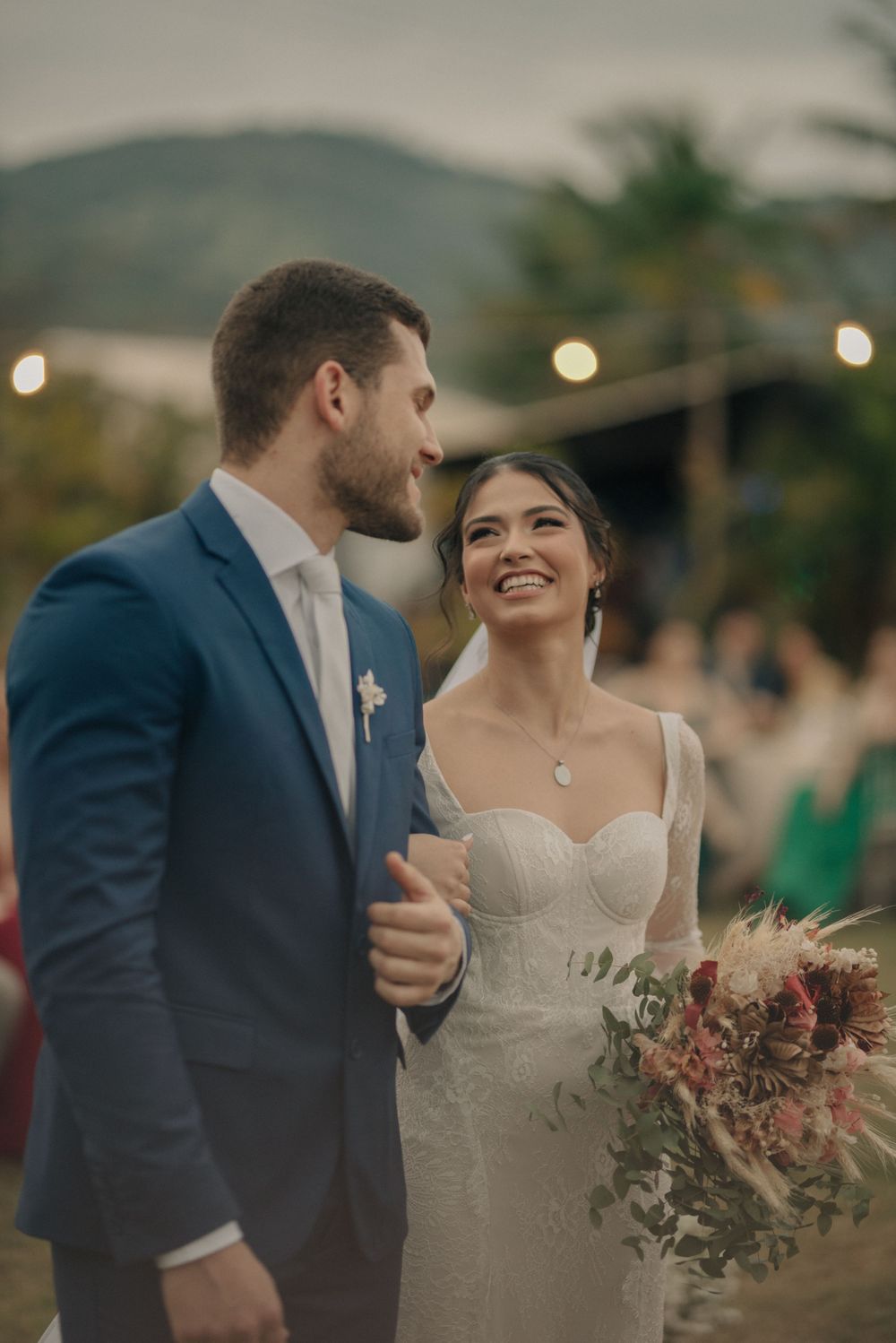 A joyful outdoor wedding celebration with mountains and string lights in the background.