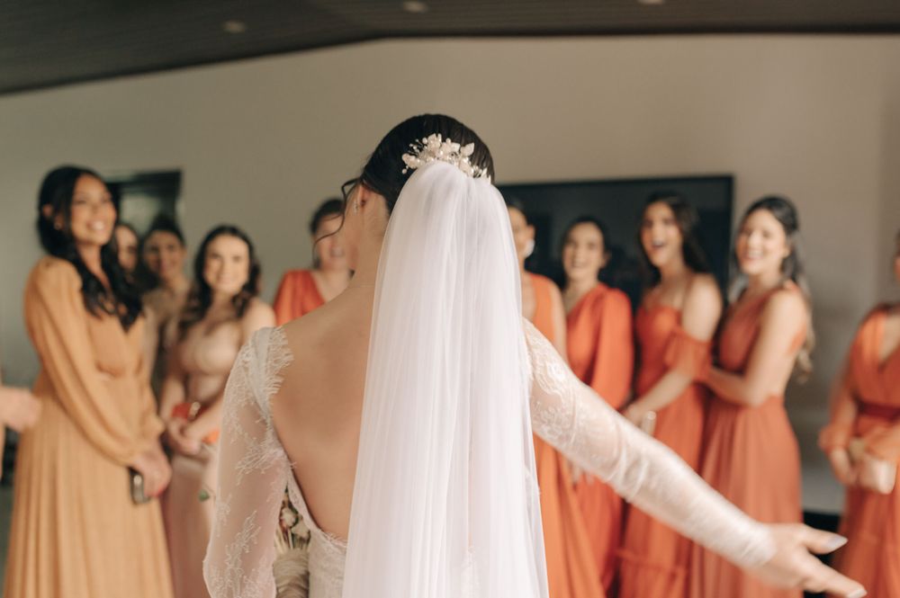 Bridesmaids in coral-colored dresses gather around during a wedding preparation moment.
