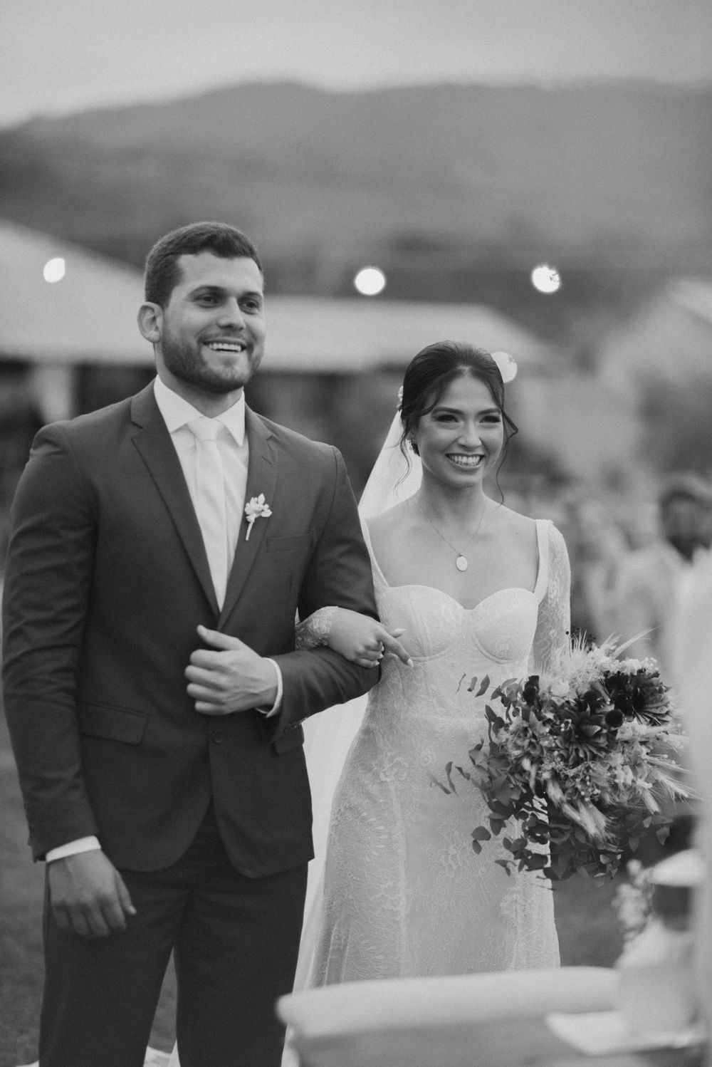 A black and white portrait of newlyweds smiling during their outdoor wedding ceremony.