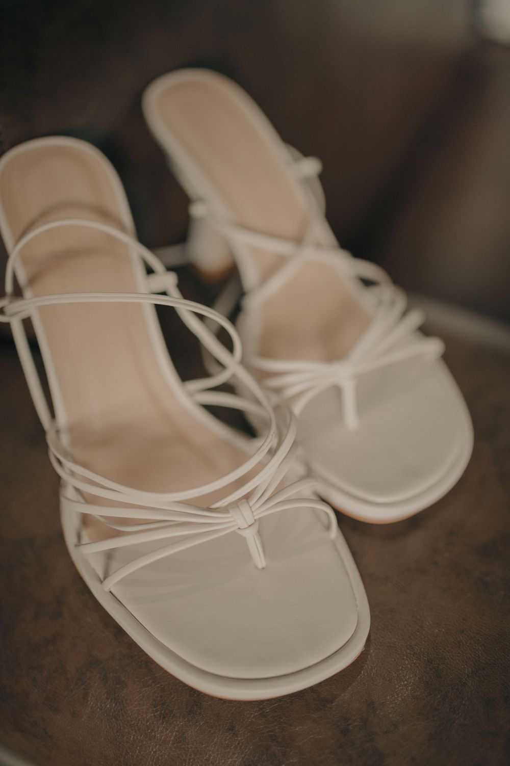 Delicate white strappy sandals with thin straps on a dark wooden surface.