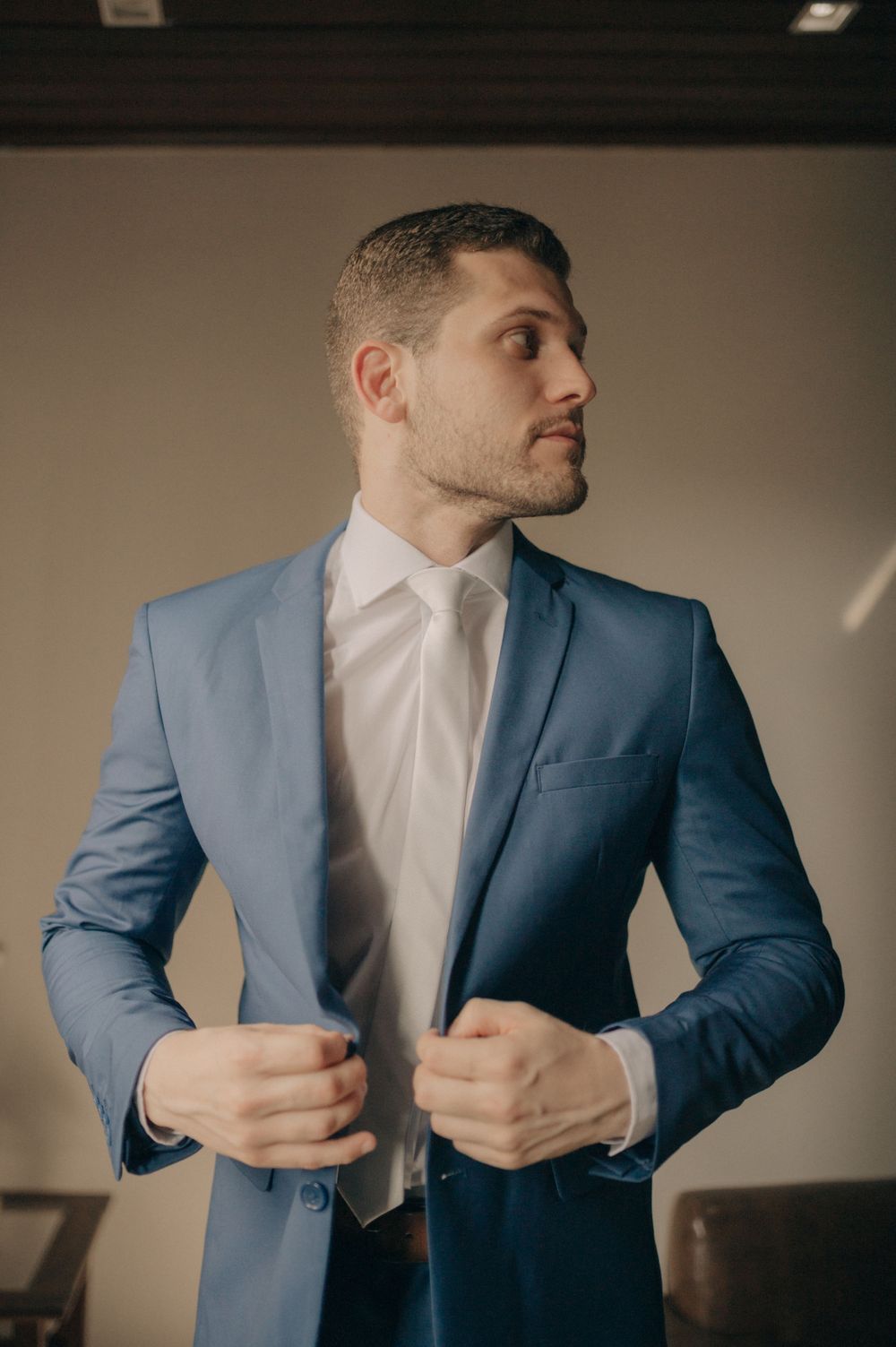 A figure wearing a tailored light blue suit jacket and white shirt adjusts their lapels.