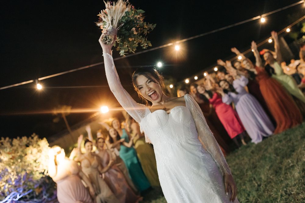 A bride raises her bouquet in celebration as wedding guests cheer in the background.