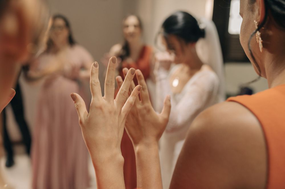 A close-up of hands showing off an engagement ring with bridesmaids in the background.