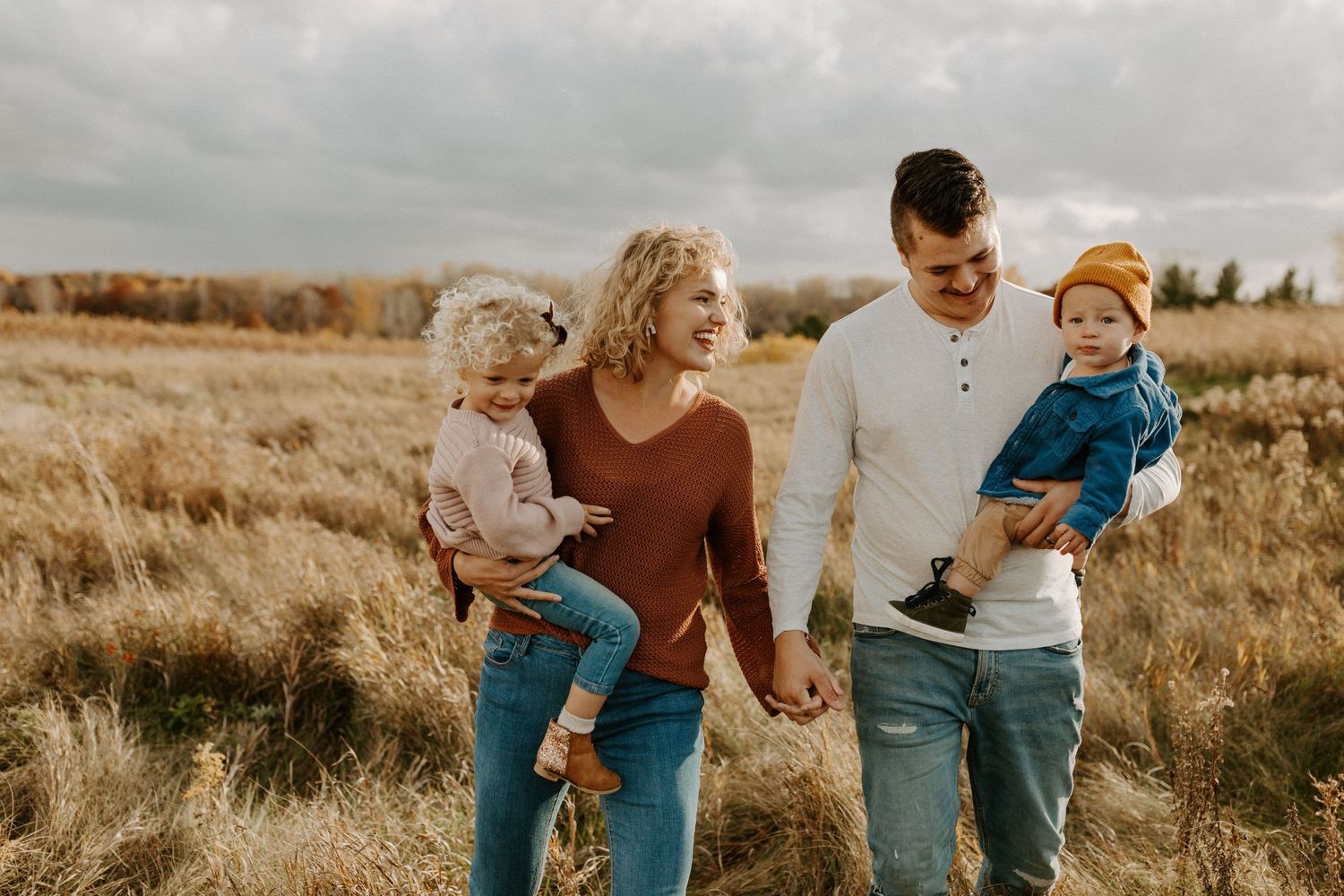 Family enjoying candid moments together in golden sunlit field during autumn photoshoot.