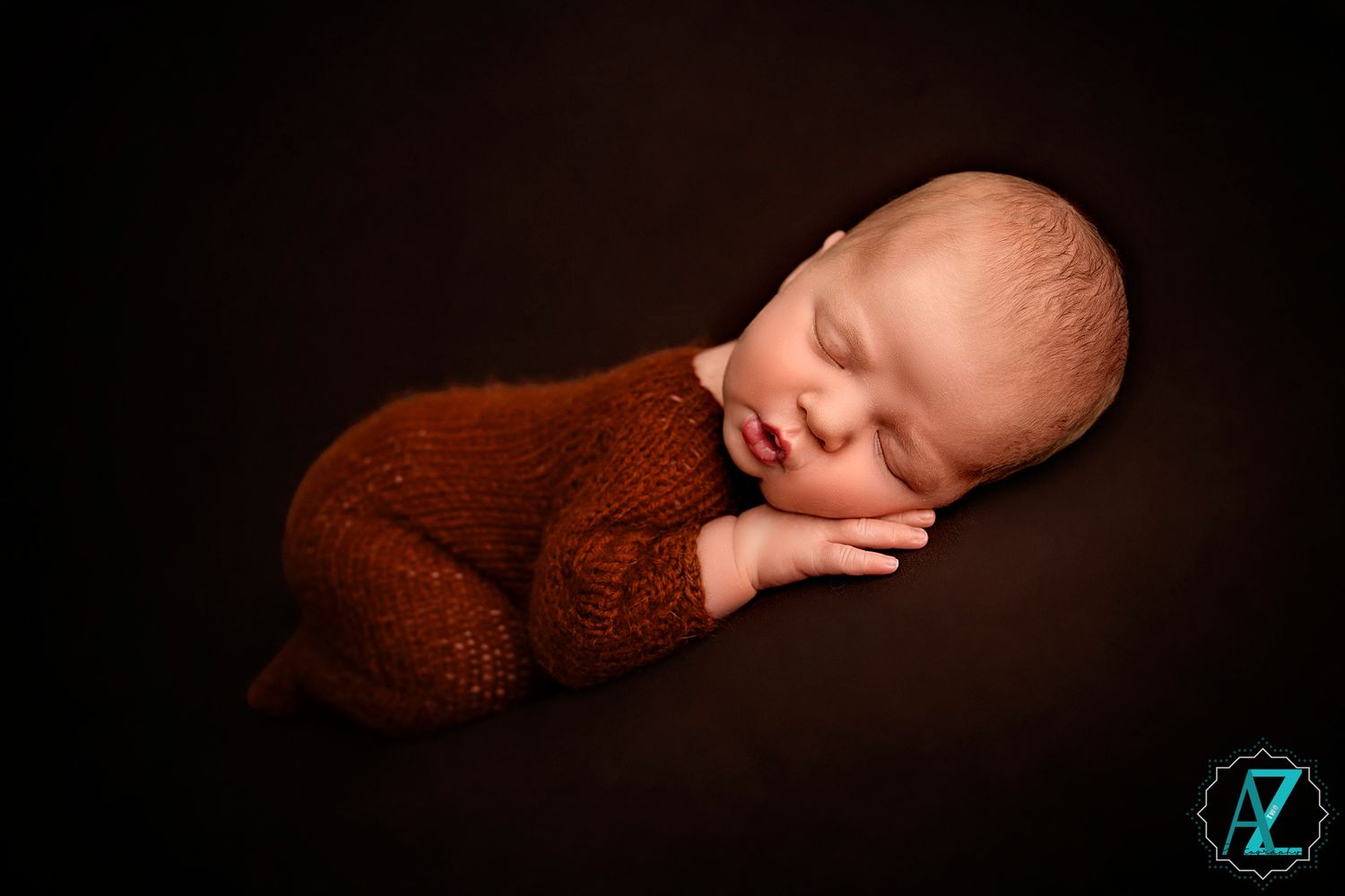 Artistic newborn portrait with baby in brown wrap against dark background.