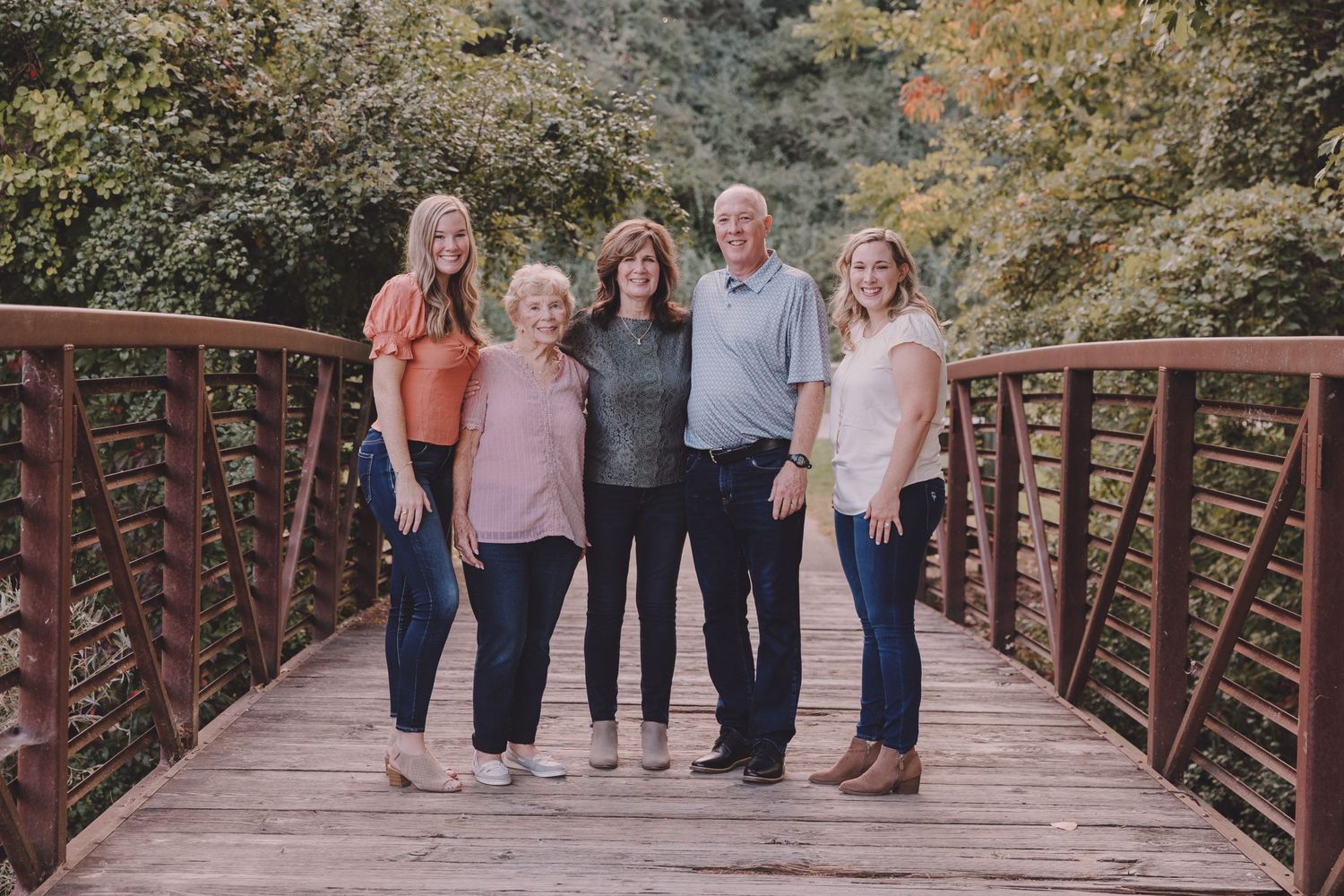 Family group portrait on a rustic wooden bridge with autumn foliage in the background.