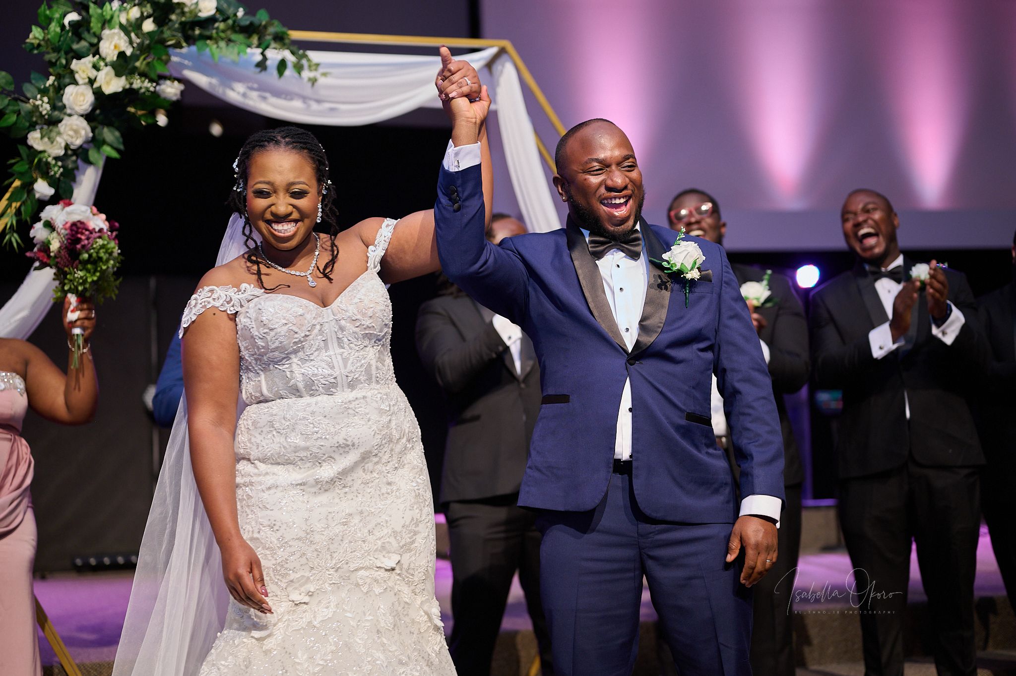 Joyful celebration moment during a wedding ceremony with raised hands under floral arch decor.