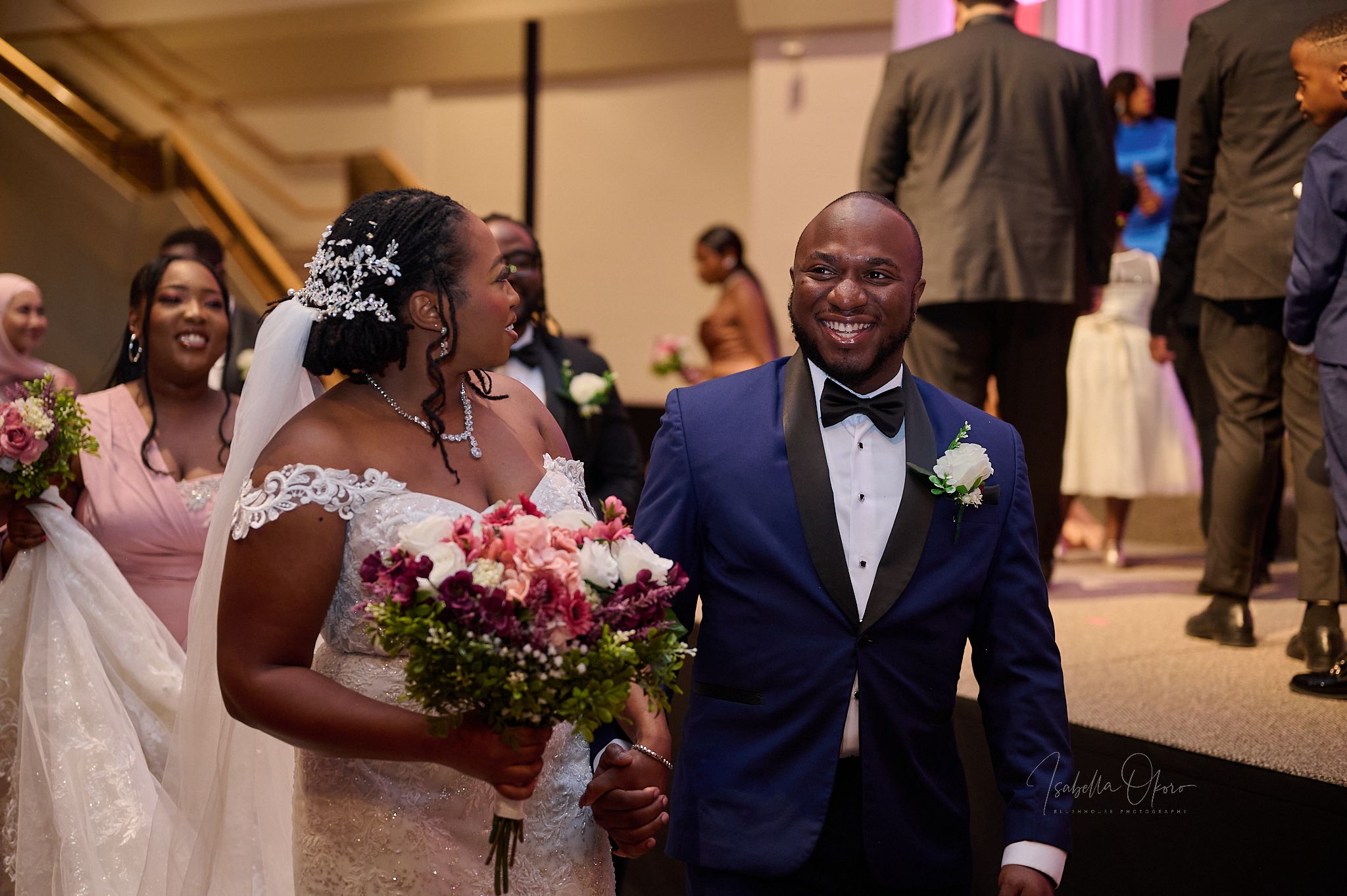 Wedding couple walks together holding pink floral bouquet during ceremony procession.