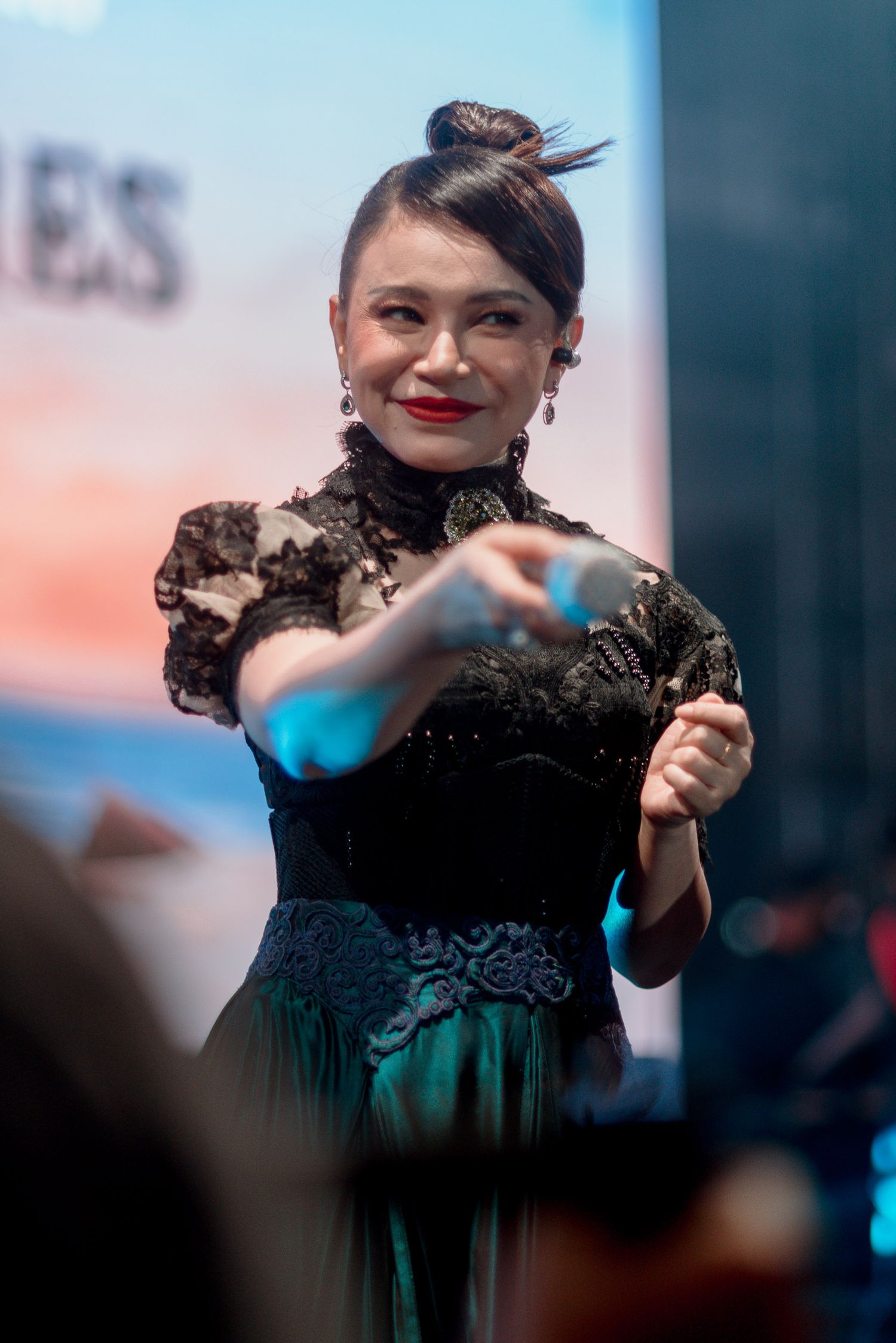 A performer in an elegant black and teal dress gestures while performing on stage.