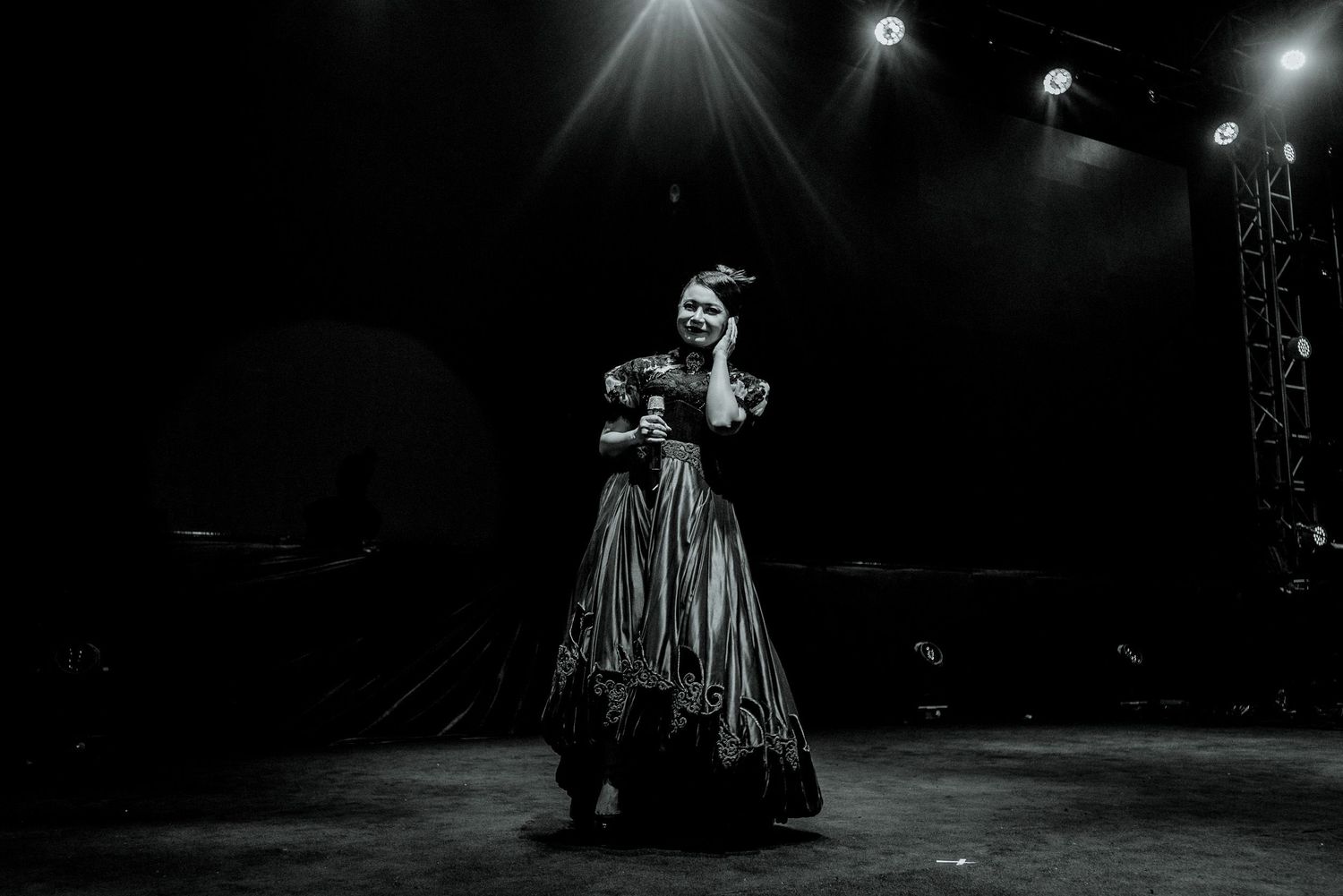 Dramatic black and white stage performance featuring a performer in a vintage-style dress under theatrical lighting.
