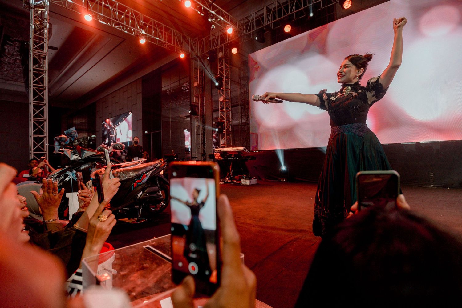 Concert performer in dark dress on stage while audience members capture the moment on phones.