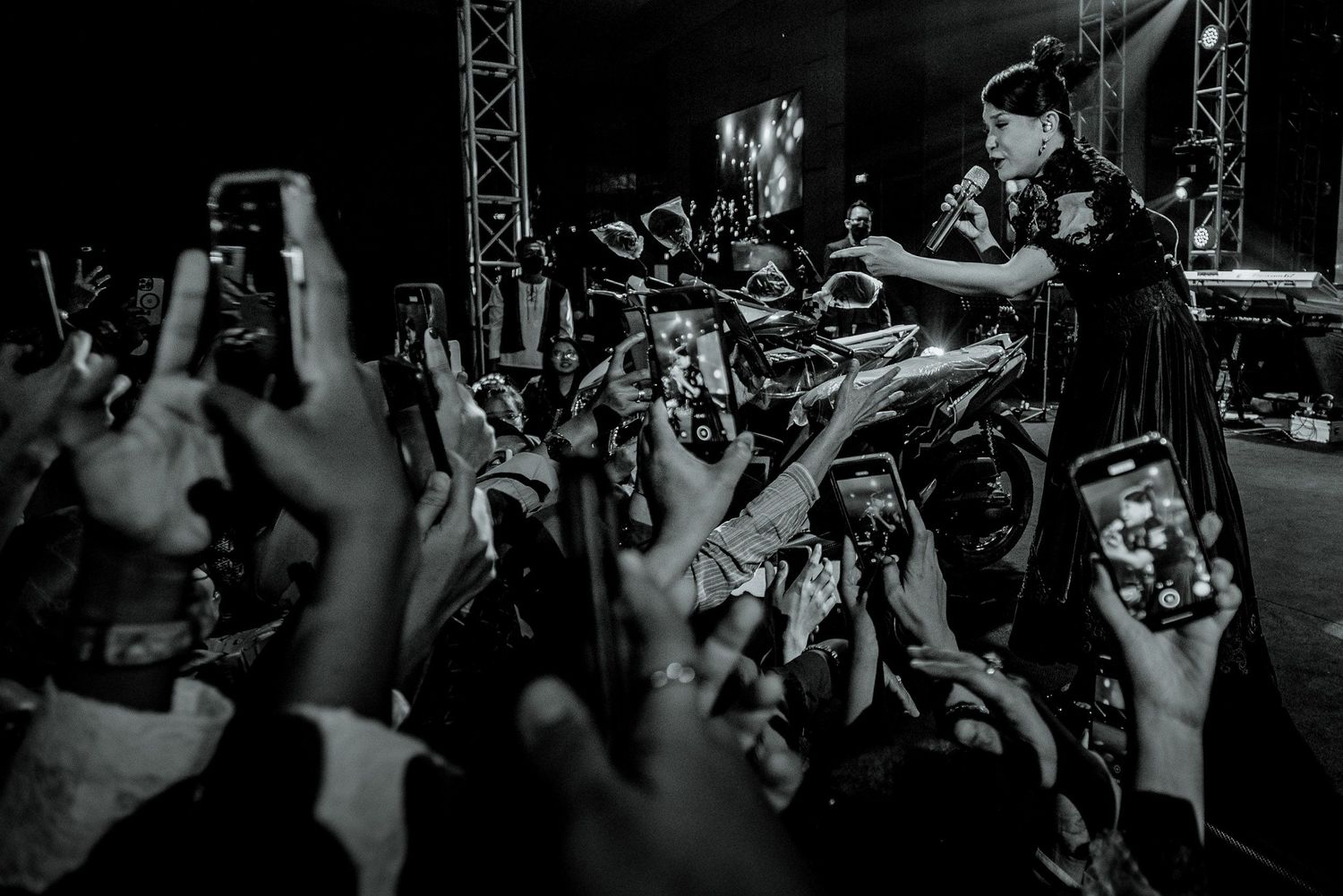 Black and white concert photo capturing crowd interaction with raised hands and phones.