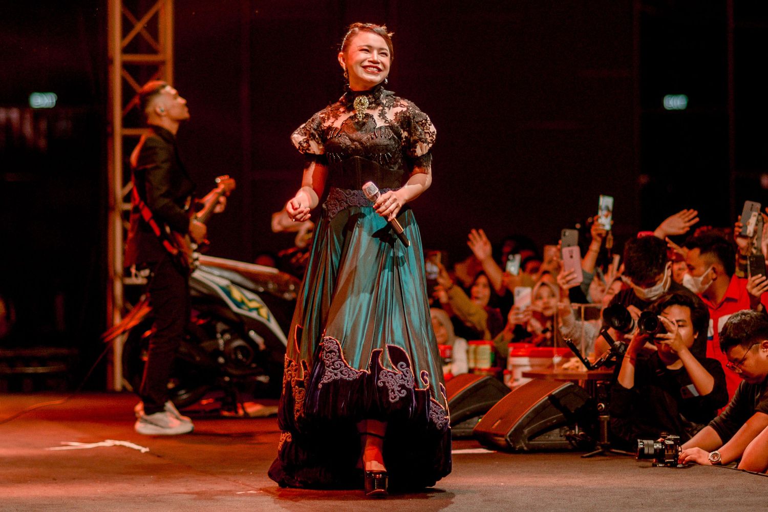 Stage performer in teal and black Victorian-style dress performing for enthusiastic crowd.