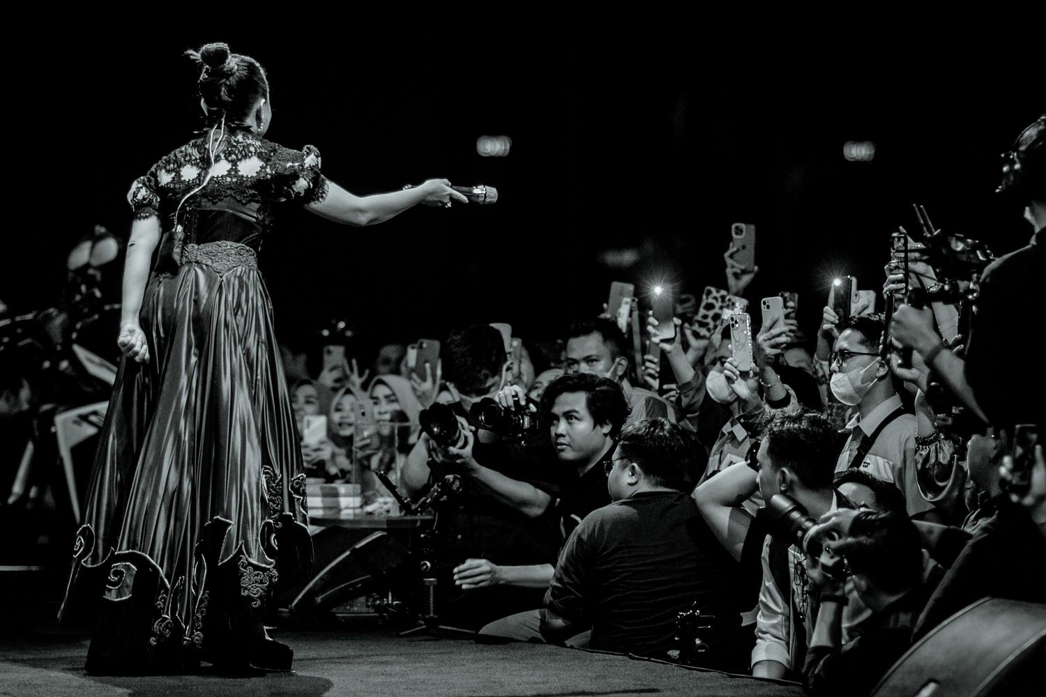 Black and white photo of stage performance with audience members reaching upward.
