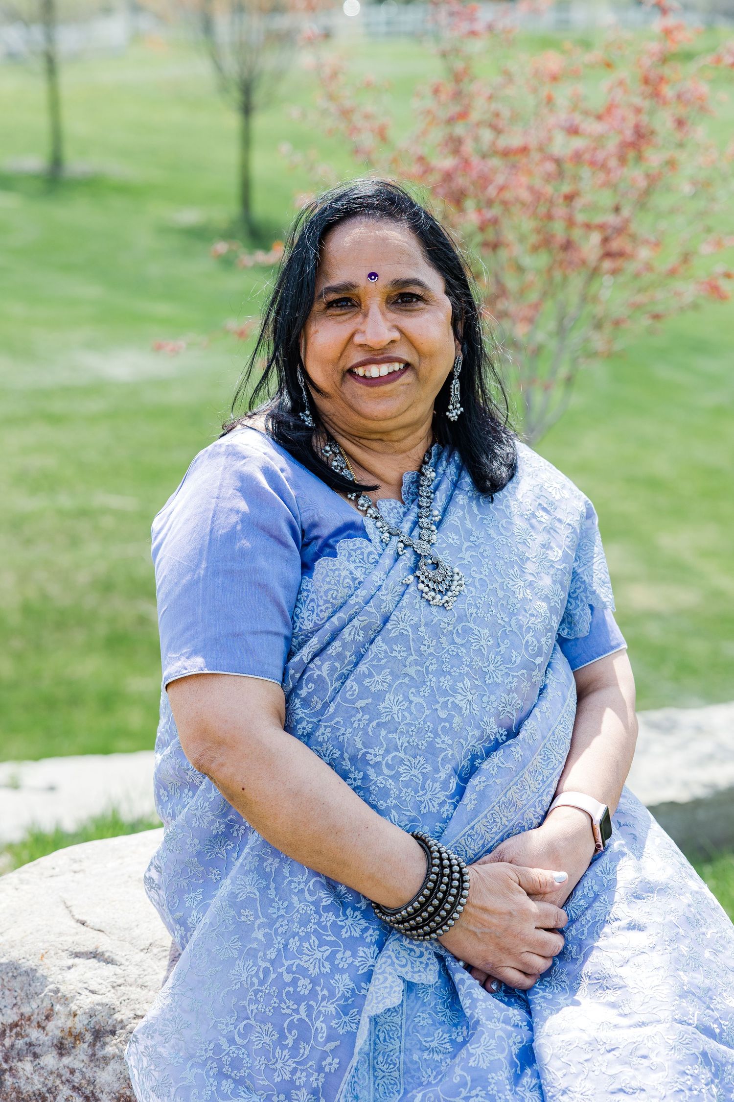 A woman in traditional Indian attire poses outdoors near autumn foliage.