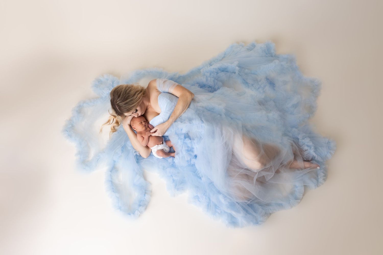 Artistic maternity photo with flowing blue fabric against white background.