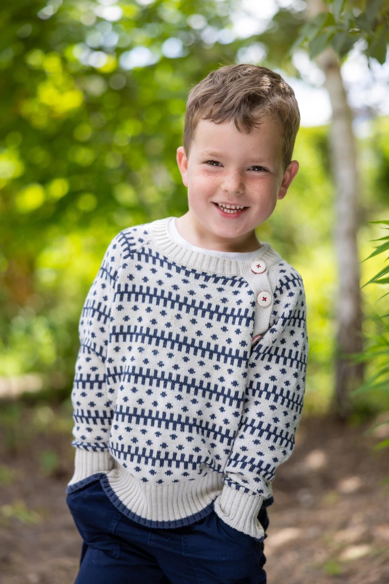 Child wearing blue and white patterned sweater smiling outdoors.
