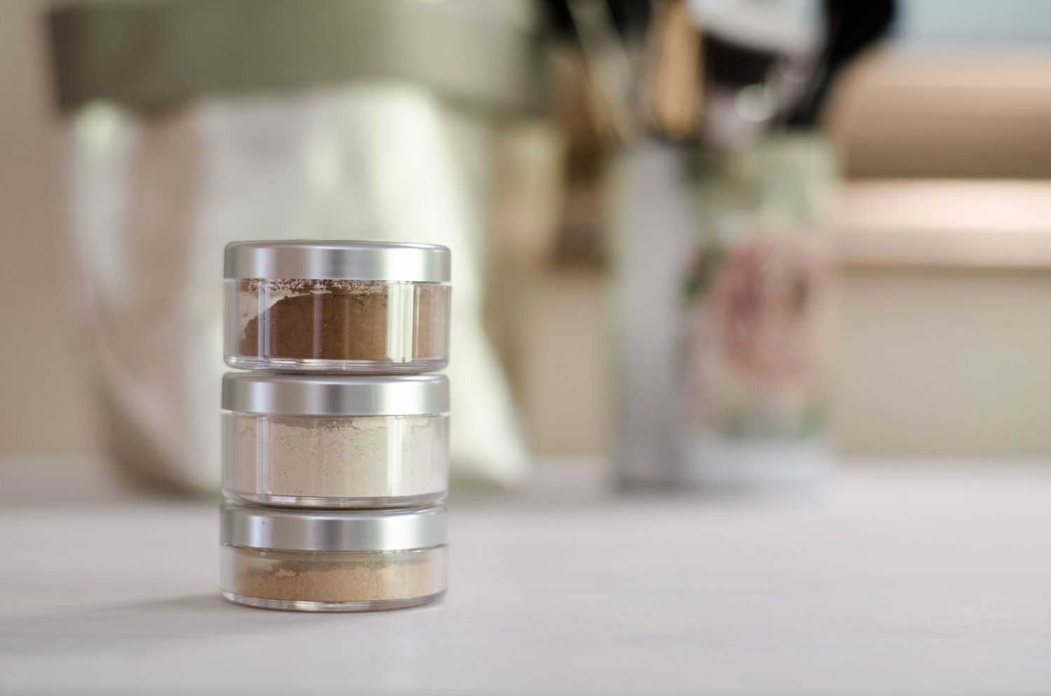Metallic makeup containers displayed on white surface with blurred background.